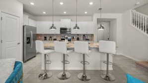 A modern kitchen with white cabinets, stainless steel appliances, and pendant lighting. - 5BR Resort Near Disney -  Sleeps 10 - Private Pool (Davenport)