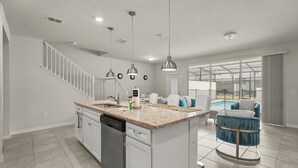 A modern kitchen with a dishwasher, granite countertop, pendant lights, a staircase, and a view of a pool. - 5BR Resort Near Disney -  Sleeps 10 - Private Pool (Davenport)