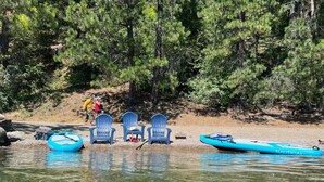 Une rive avec des chaises, un kayak et une personne qui se promène.