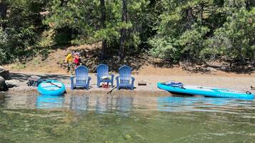Une rive avec des chaises, un kayak et une personne qui se promène.