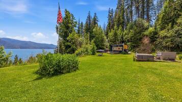 Un chalet offrant une vue sur un lac et des montagnes, entouré d’arbres et doté d’une pelouse bien entretenue.