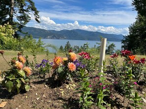 Ein Garten mit bunten Blumen und Blick auf einen See und Berge.