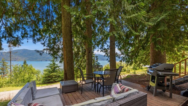 A deck with outdoor furniture, a grill, and a view of a lake and mountains.