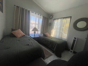 Ein Zimmer mit zwei Betten, einer Lampe, einem Heizgerät und einem Fenster mit Vorhängen.