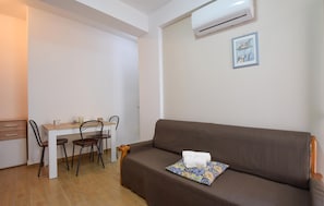 Ein Zimmer mit einem braunen Sofa, einem kleinen Tisch mit Stühlen, einer Klimaanlage und einem gerahmten Bild an der Wand.