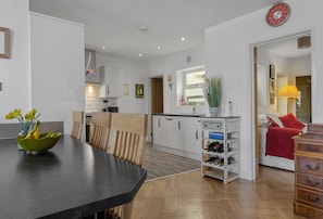 A modern kitchen with white cabinets, a dining area with a black table, and a living space with a red sofa. - Harbour View at No.11, an exceptional coastal holiday home in Brixham (Brixham)