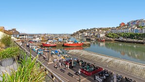 Um porto com barcos, um calçadão à beira-mar e edifícios ao fundo.