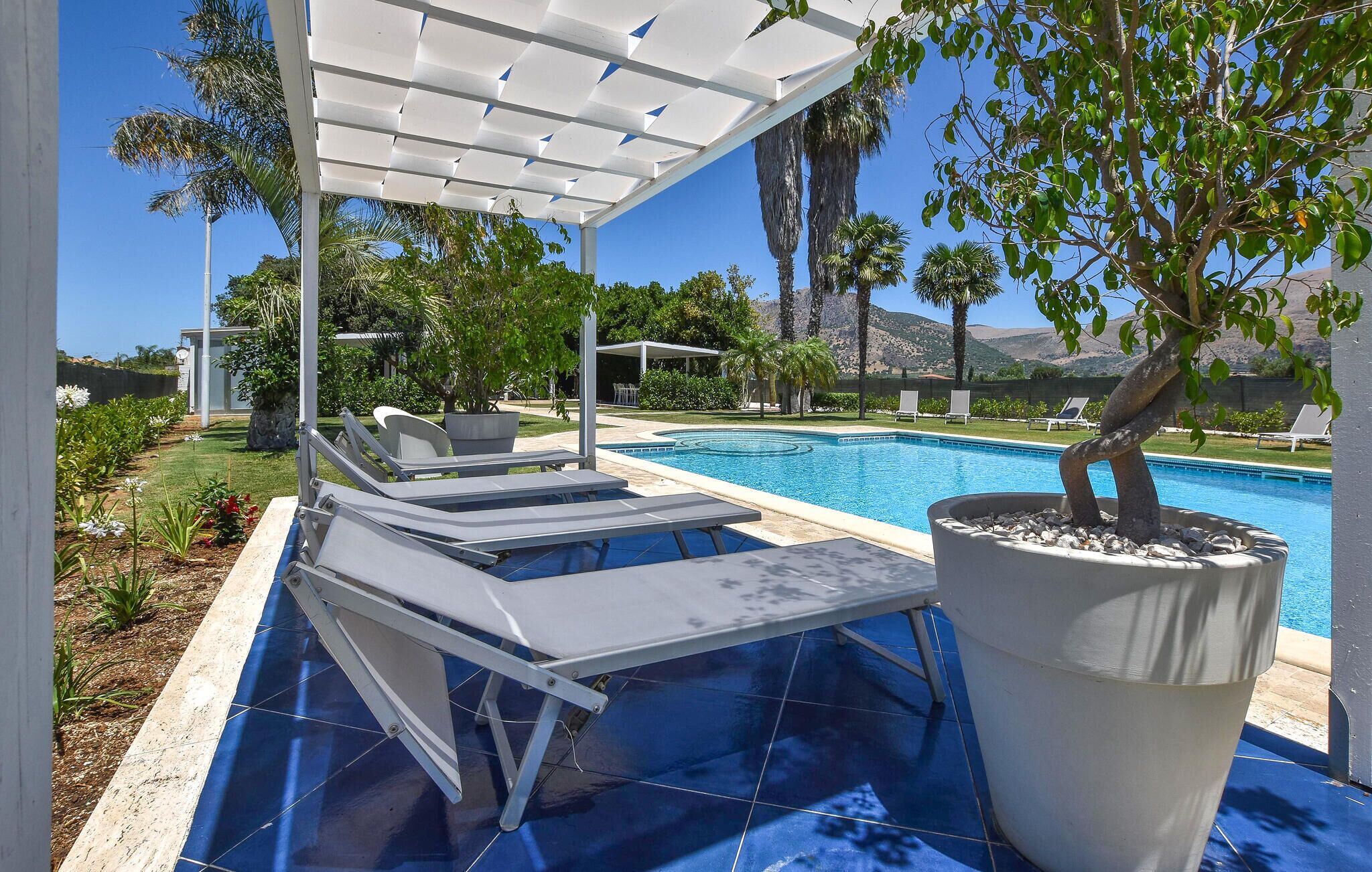 Un espace aménagé au bord de la piscine, avec des chaises longues, une pergola et un arbre en pot.