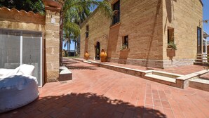 A courtyard with a brick pathway, a white bench, and a building with a textured facade. - Nice home in Partinico (Partinico)