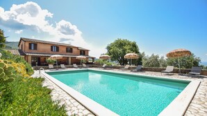 A swimming pool with lounge chairs and umbrellas, a building with a tiled roof, and a clear sky. - Amazing home in Montecchio (Montecchio)