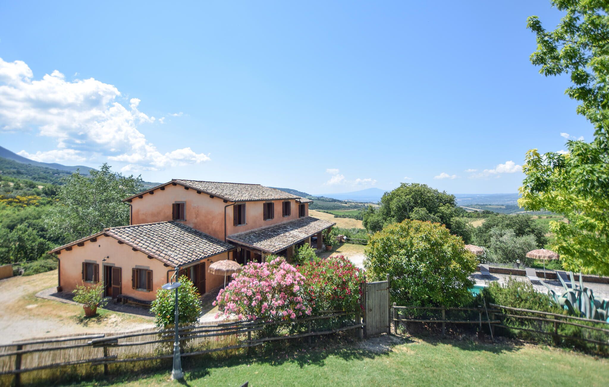 A rustic two-story house with a tiled roof, surrounded by lush greenery and a clear view of the countryside.
