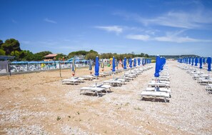 Ein Strand mit Reihen aus weißen Liegestühlen und blauen Sonnenschirmen.
