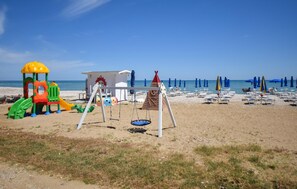 Ein Strand mit einem Spielbereich für Kinder, Strandstühlen und Liegen.