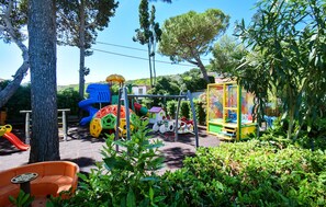 Un parque infantil con diversas estructuras de juego, rodeado de follaje y árboles.