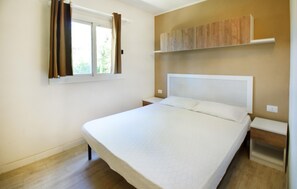 Ein Schlafzimmer mit Bett, einem Fenster mit Vorhängen, einem Nachttisch und einem Einbauschrank.
