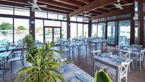 Un espace extérieur abrité, aménagé pour les repas, avec des tables et des chaises, de grandes fenêtres et des ventilateurs de plafond.