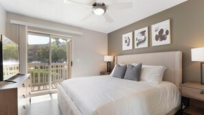 A hotel room with a large bed, a ceiling fan, a TV, and a balcony with a view of the outside. - Landing Furnished Apartments - Northwest Austin (Austin)
