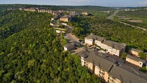 An aerial view of a residential area with multiple apartment buildings, surrounded by dense forest, and a clear sky. - Landing Furnished Apartments - Northwest Austin (Austin)