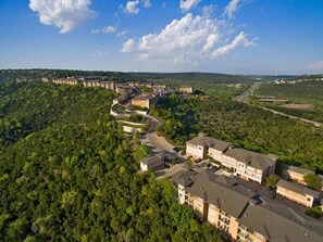 Luftaufnahme eines Wohngebiets mit mehreren Mehrfamilienhäusern, umgeben von dichtem Wald und blauem Himmel.