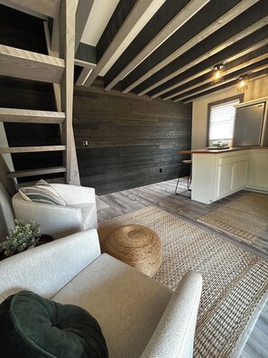 A loft-style room with exposed beams, a built-in kitchen, and a cozy seating area with a sofa and ottoman. - The Backyard Hideout (Mancos)