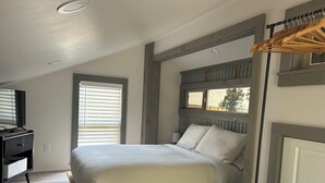 Une chambre à coucher avec un lit, une télévision, une fenêtre et un plancher en bois.