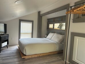 A bedroom with a bed, a TV, a window, and a wooden floor. - The Backyard Hideout (Mancos)