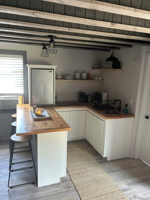 A compact kitchen with white cabinetry, a wooden countertop, and a built-in sink. There are bar stools, a coffee maker, and a kettle on the counter. - The Backyard Hideout (Mancos)