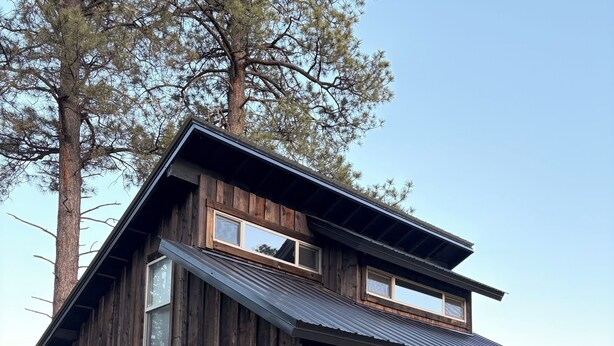 Une maison rustique en bois, à deux étages, dotée d’un porche couvert et d’un petit jardin à l’avant.