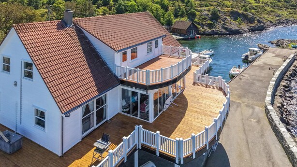 A two-story house with a red-tiled roof, a wooden deck, and a view of a body of water.
