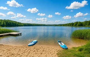 A calm lake with two paddleboards on the shore, surrounded by lush greenery and a clear sky.