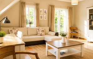 Ein gemütliches Wohnzimmer mit einer Couch, einem Holztisch, einem Sessel, einer Lampe und einem Bücherregal.