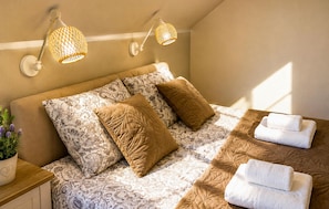 Ein Schlafzimmer mit einem Bett, zwei Wandlampen, einem Nachttisch mit Pflanze und einem Fenster, das natürliches Licht hereinlässt.