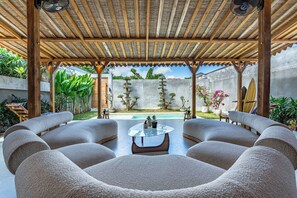 A covered outdoor seating area with a pool view, featuring a round glass table and cushioned chairs. - Brand New - 2bdrs: Luxury, Concierge & Security (Badung)
