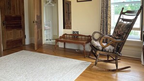 A room with a wooden rocking chair, a small table, a white rug, a wooden door, a white closet, and a window with curtains. - Charming East View overlooks College Green Park (Iowa City)