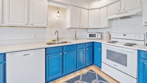 Cucina con pensili bianchi, basi blu, lavastoviglie, forno a microonde e forno.