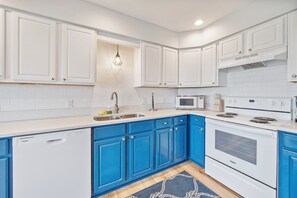 Eine Küche mit weißen Schränken, blauen Unterschränken, einem Geschirrspüler, einer Mikrowelle und einem Backofen.