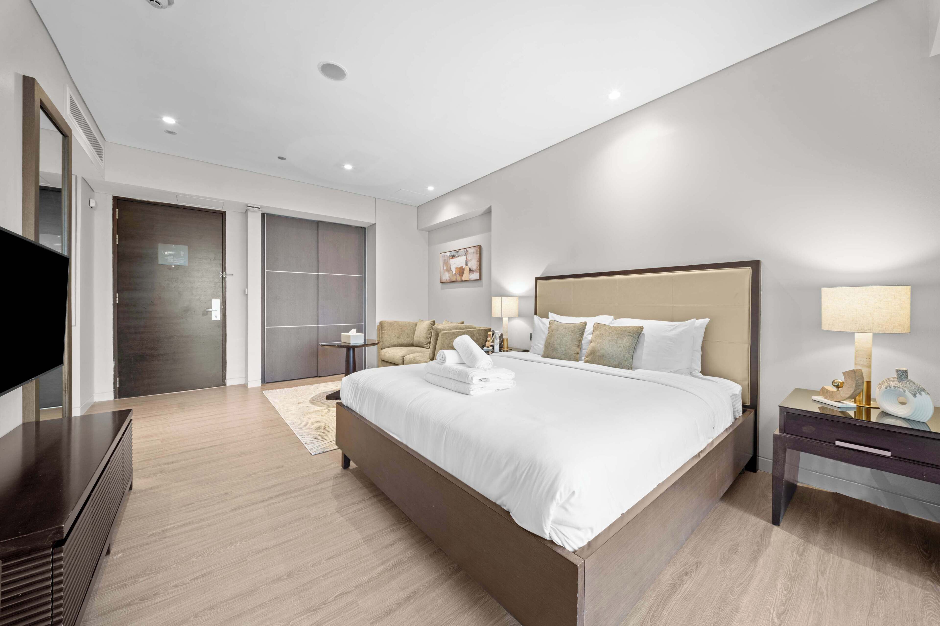 A modern hotel room with a large bed, a flat-screen TV, a bedside table, and a wardrobe.