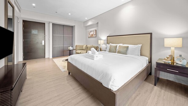 Quarto de hotel moderno com uma cama grande, televisão de tela plana, mesa de cabeceira e guarda-roupa.