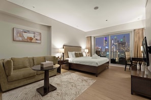 A hotel room with a bed, a sofa, a desk, a chair, a TV, and a view of a cityscape at night. - Chic Studio JW Marriott Dubai Marina (Dubai)