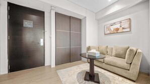Uma sala de estar moderna com uma porta de madeira escura, um sofá bege, uma mesa de centro de vidro e um tapete estampado.