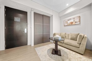 Ein modernes Wohnzimmer mit einer dunkelholzenden Tür, einem beigefarbenen Sofa, einem Glastisch und einem gemusterten Teppich.