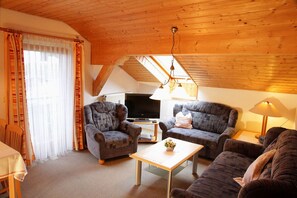 A cozy living room with a wooden ceiling, two patterned sofas, a television, and a table with a lamp. - Vacation Apartment 1 with a balcony for 4 people, 2 separate... Bedroom (Seebruck)