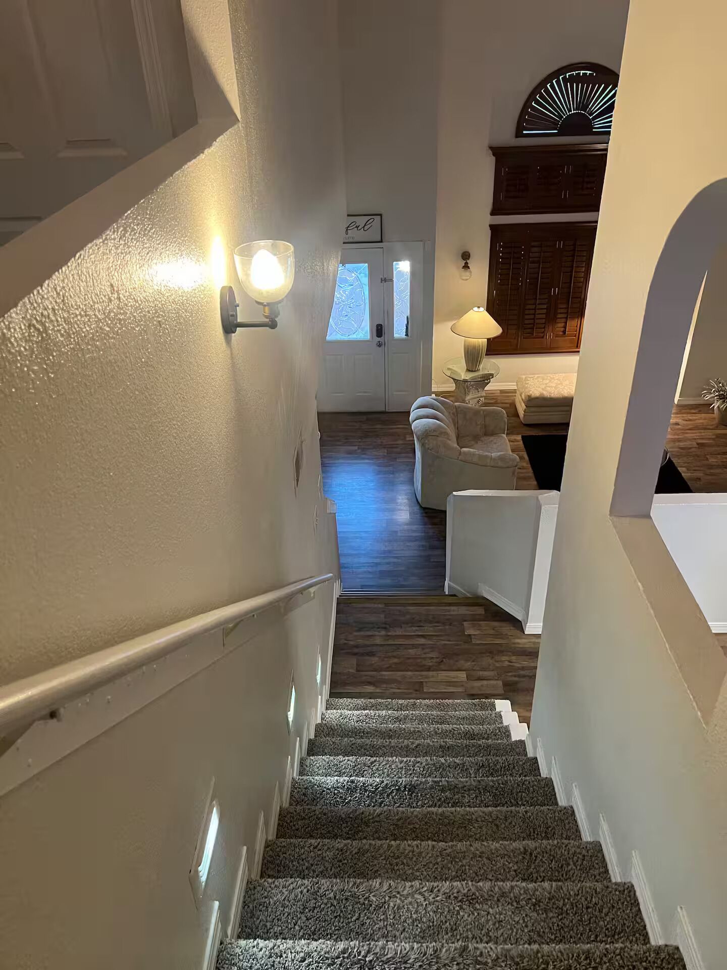 A staircase leading to a living area with a sofa, a lamp, and a decorative wall.