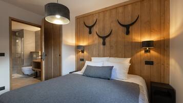 A bedroom with a wooden headboard, two wall-mounted lamps, a bed with white and gray bedding, and a hanging light fixture.