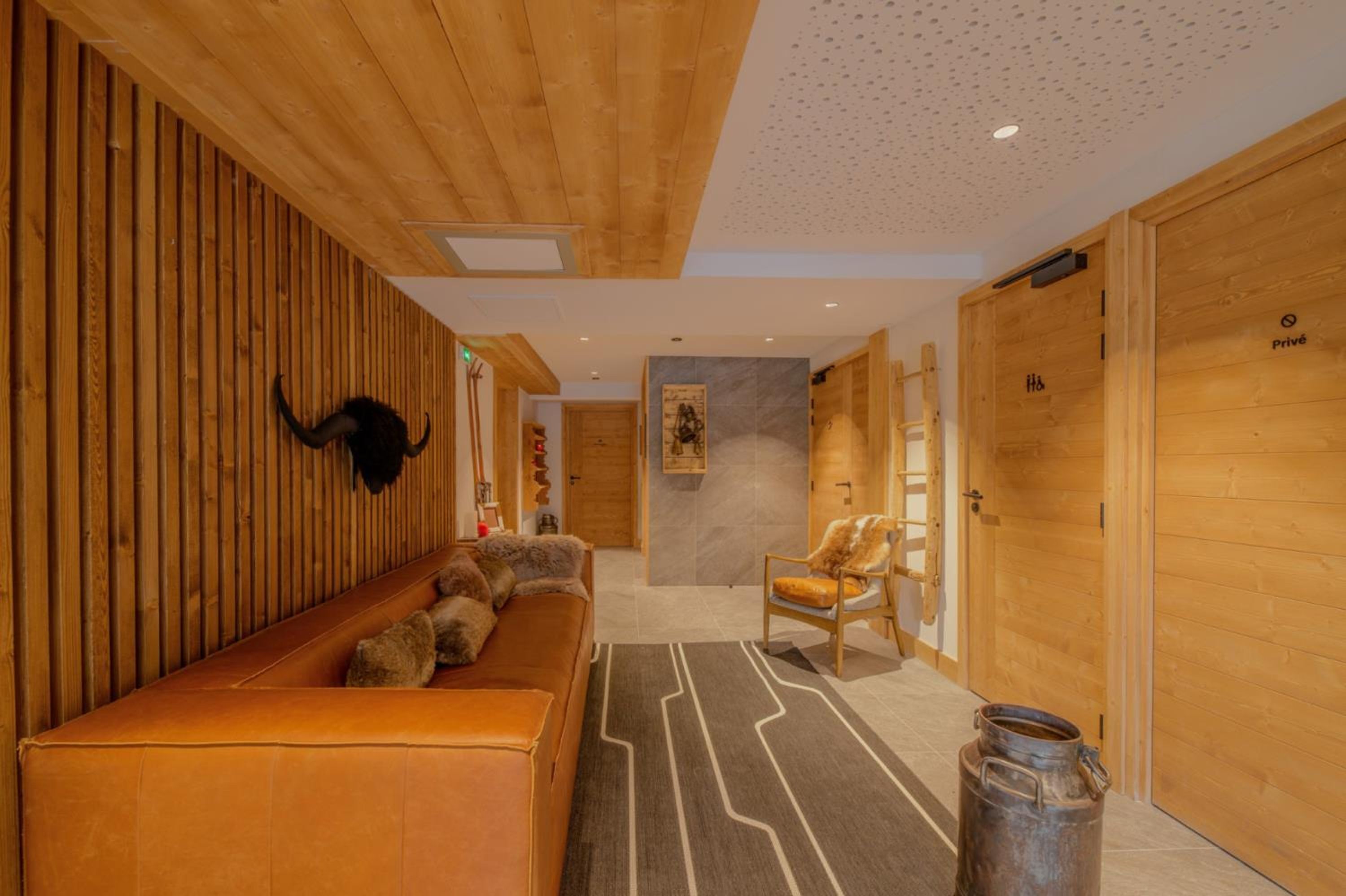 A wooden interior with a bench, a chair, and a large metal container.