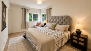 Ein Schlafzimmer mit einem großen Bett, zwei Nachttischen, einem Fenster mit Vorhängen und einer Deckenleuchte.