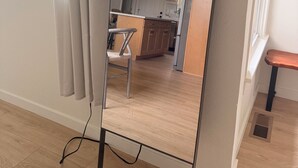 Ein modernes Zimmer mit einem großen Spiegel, Holzböden und Blick auf eine Küche und einen Essbereich.