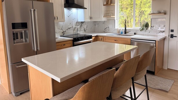 Eine moderne Küche mit einer großen Kochinsel, Edelstahlgeräten, einer Marmor-Spritzschutzwand und Holzschränken.