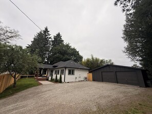 A two-story house with a gravel driveway, a wooden fence, and a garage. - 3-bedroom house in Vancouver with large yard and AC to relax (Vancouver)