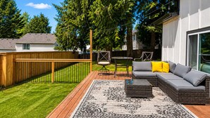 Ein Garten mit einer Holzterrasse, Gartenmöbeln und einem großen Baum.